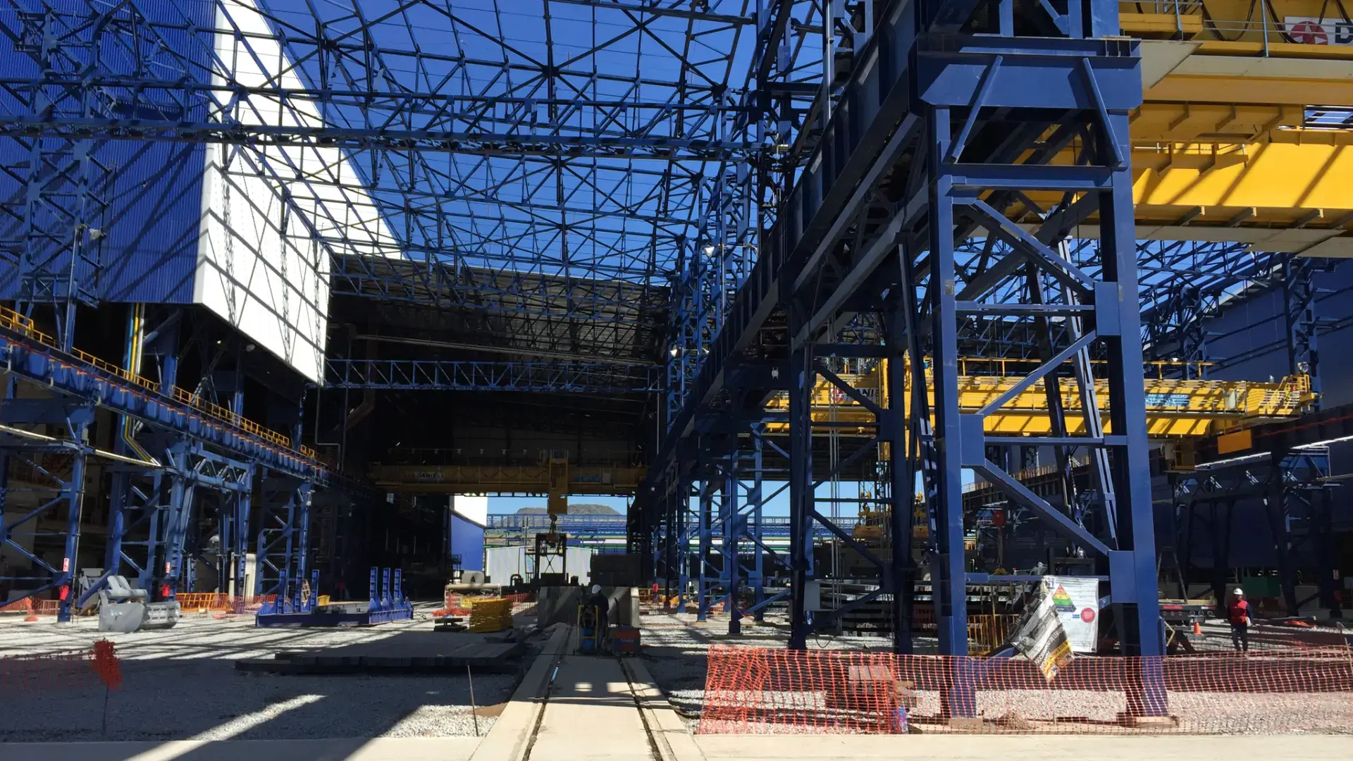 Estructura de acero azul expuesta y grúas viajeras amarillas en una nave industrial en construcción por TREBOTTI, mostrando precisión en ingeniería de detalle y coordinación de obra