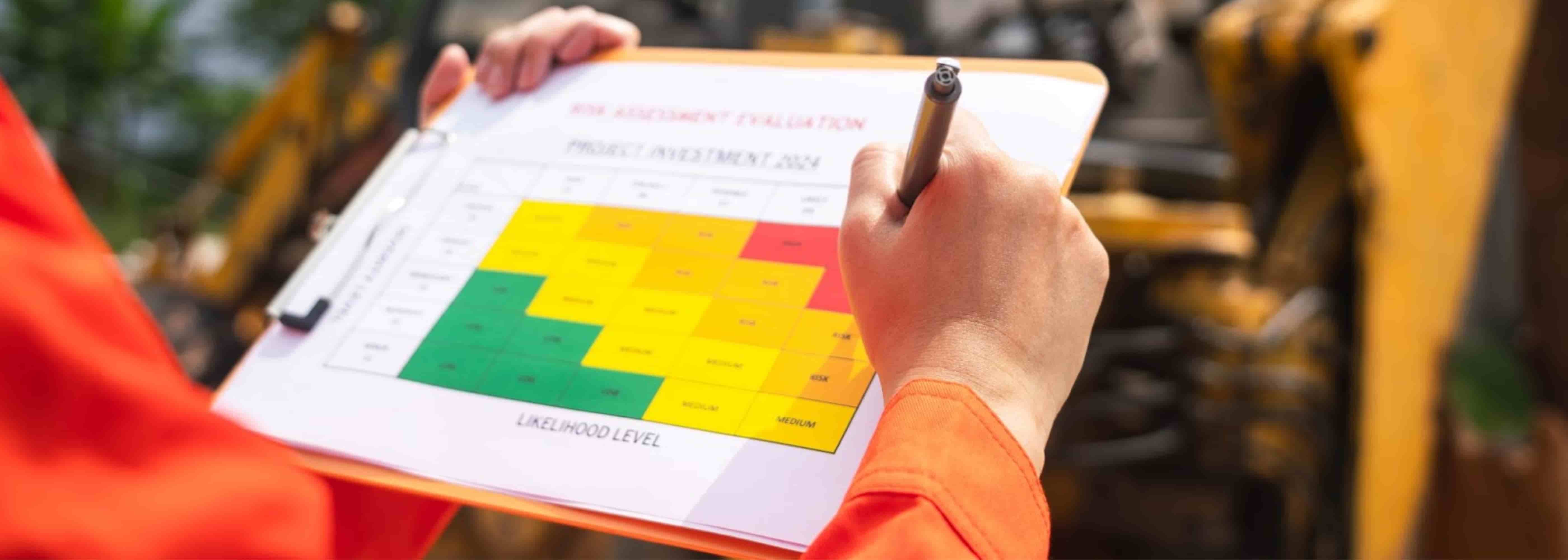 Persona con uniforme naranja sostiene un portapapeles con una matriz de evaluación de riesgos de colores (verde, amarillo y rojo) que mide niveles de probabilidad e impacto, en un entorno industrial con maquinaria al fondo.