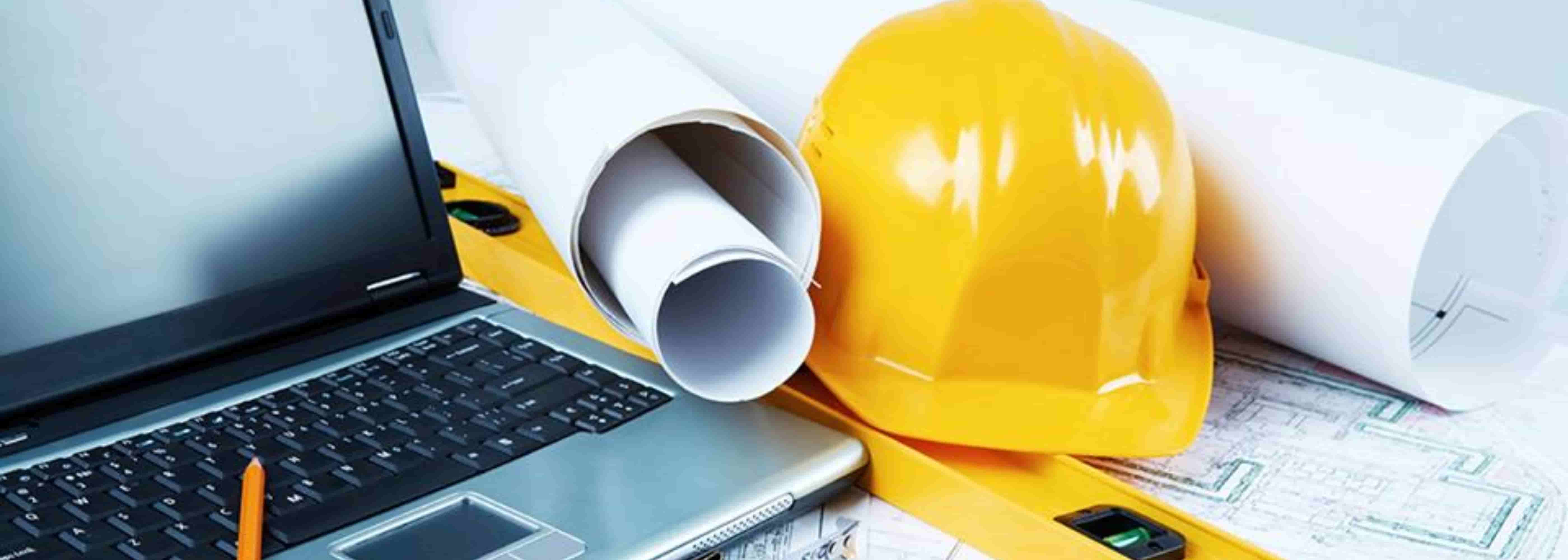 Casco de seguridad amarillo junto a planos enrollados, una computadora portátil y herramientas de construcción, simbolizando planificación y gestión de proyectos de ingeniería y construcción.